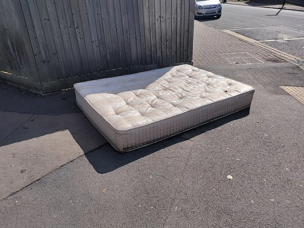 A discarded mattress beside a wooden fence in Coventry.